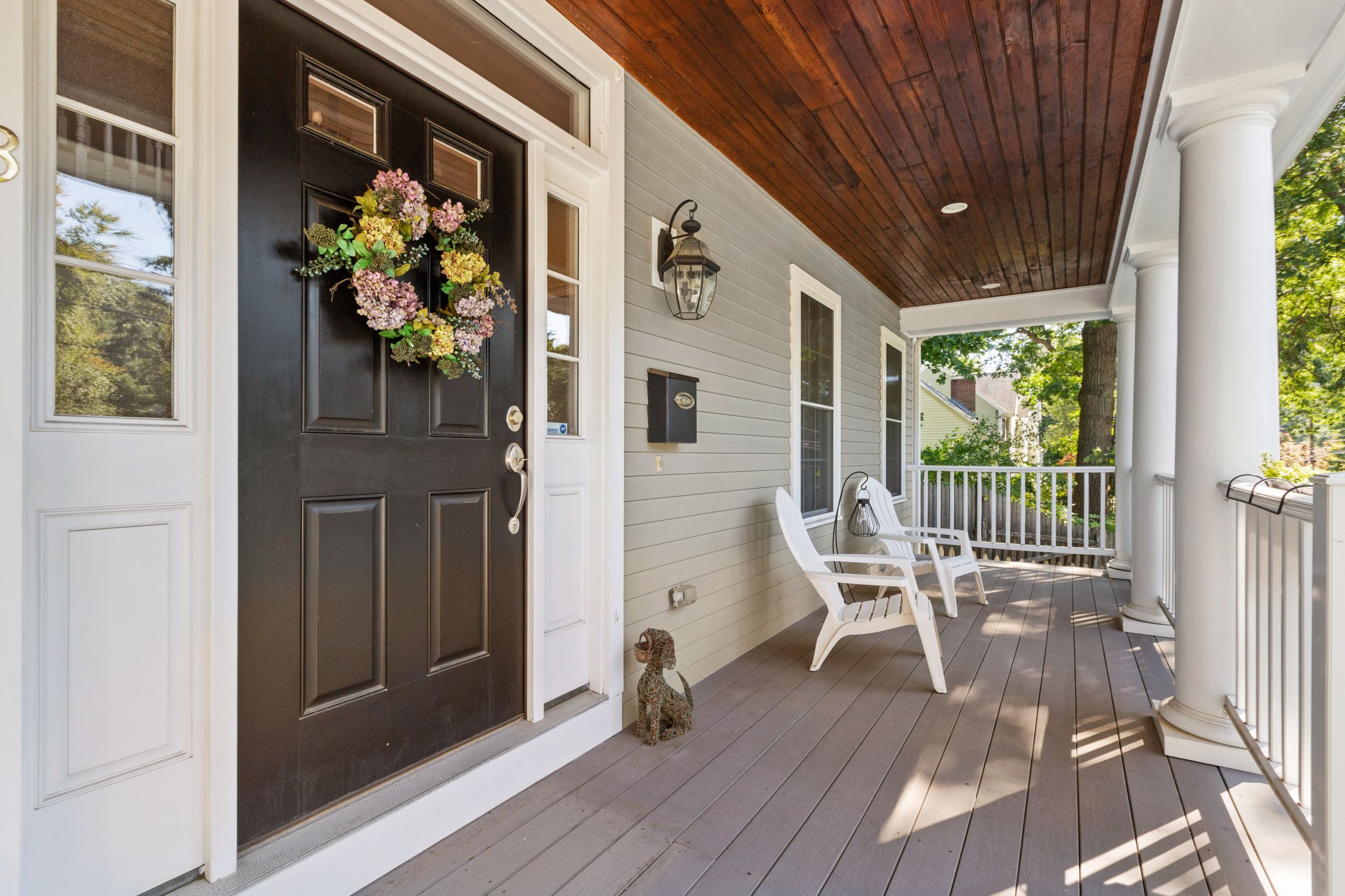Covered front porch with black door, floral wreath, white columns, wood ceiling, and seating at a Needham MA home.