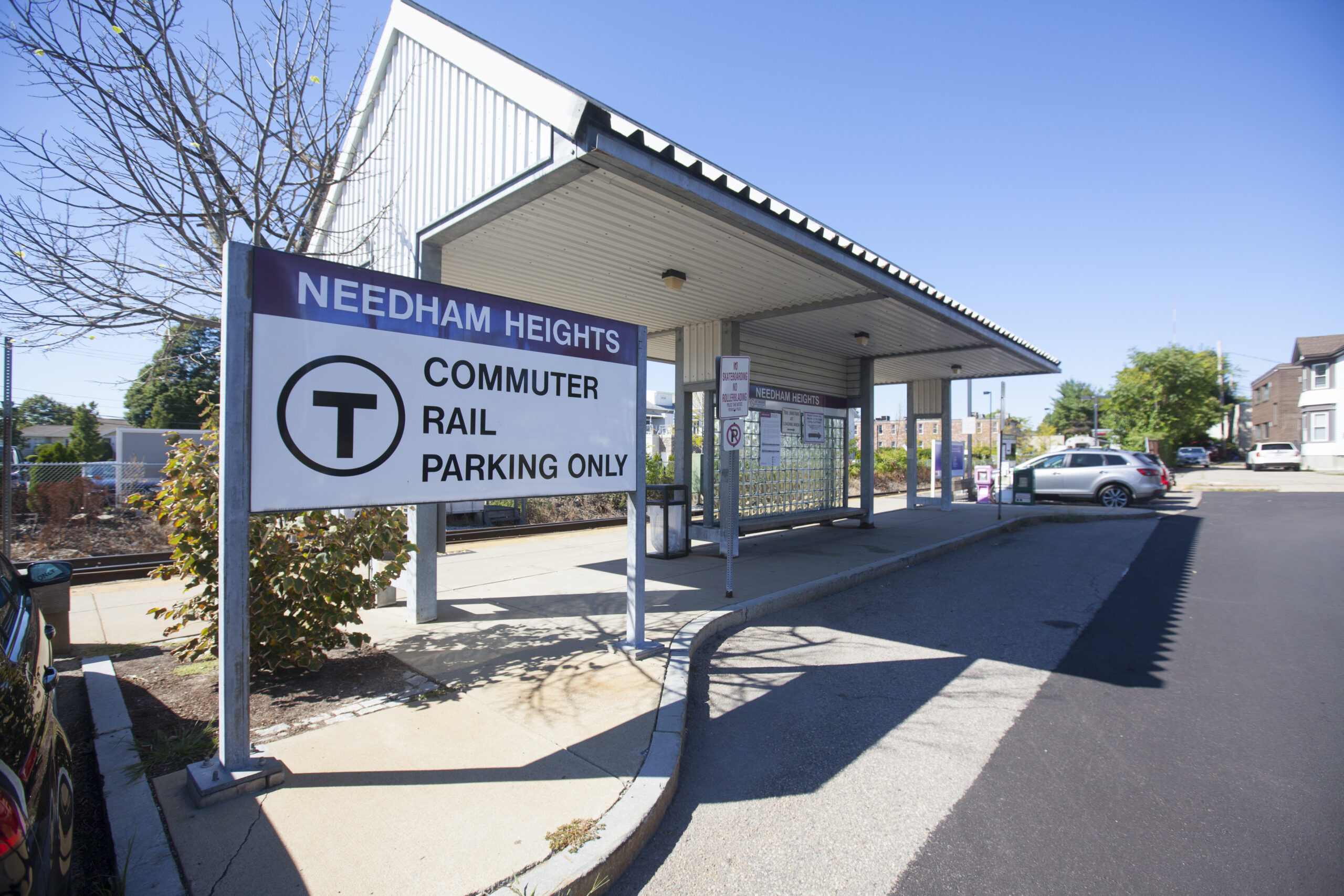 MBTA commuter rail station in Needham MA with train tracks, platform, and signage for Boston-area public transportation.