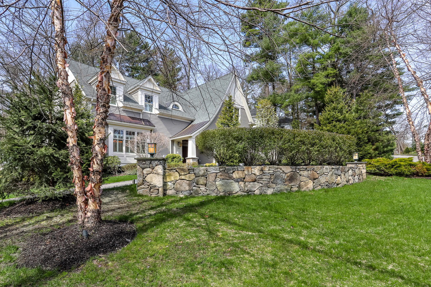 ALT text: Luxury gray shingle-style home with white trim, dormer windows, stone walkway, and landscaped front yard in Wellesley MA.