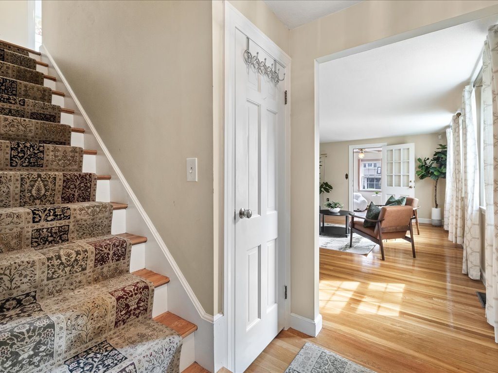 Entryway in a Needham, MA, home featuring a patterned stair runner, hardwood floors, and an open view into a bright living room.