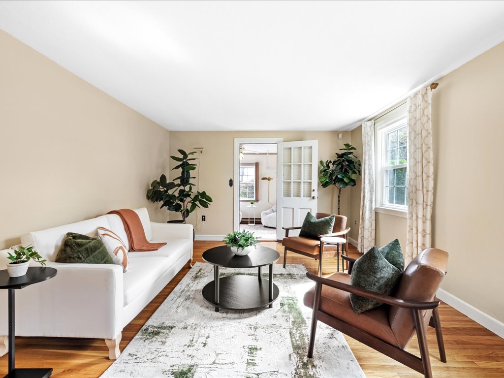 Bright living room in Needham, MA, featuring a white sofa, brown leather chairs, hardwood floors, large windows, neutral walls, and green accent pillows.