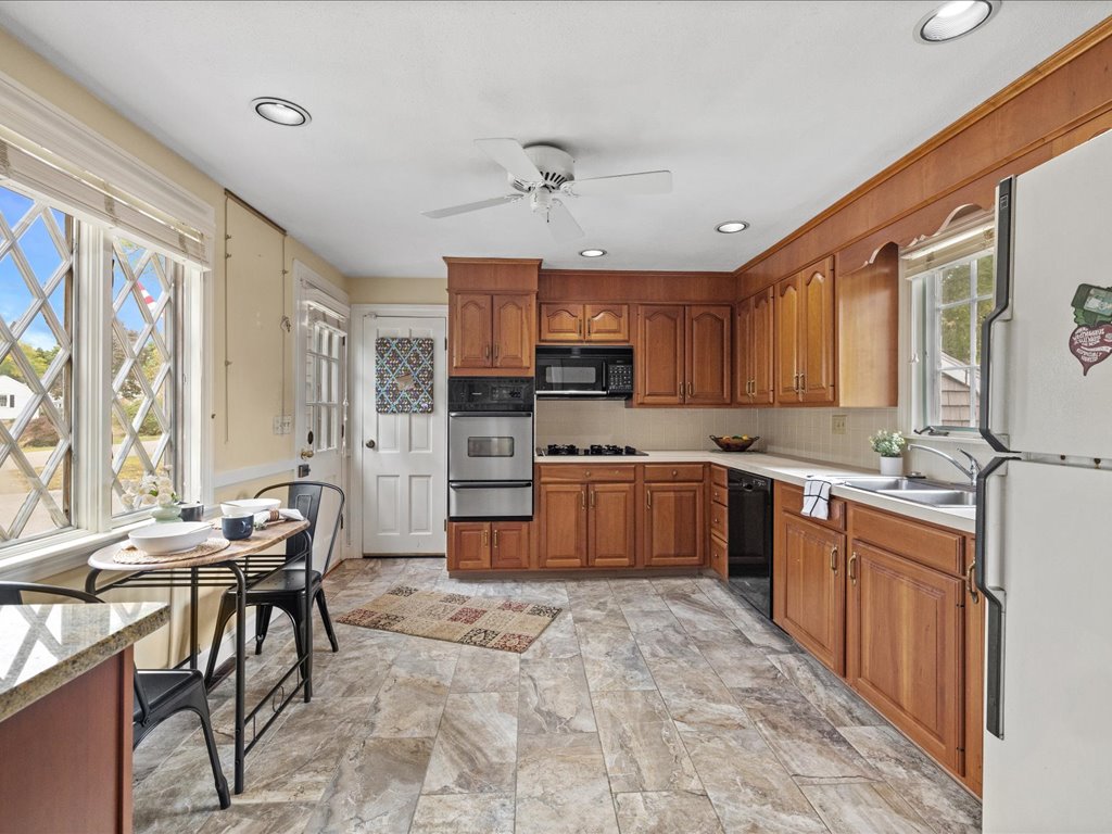 Kitchen in Needham, MA, featuring warm wood cabinetry, tile flooring, white appliances, a breakfast table, and abundant natural light from large windows.