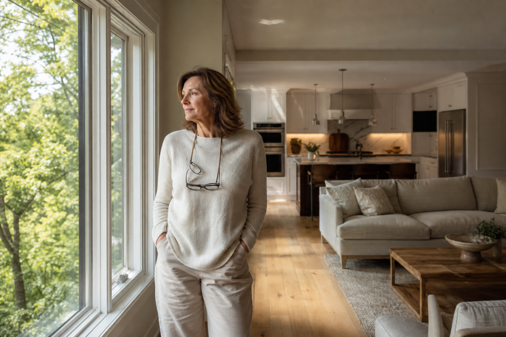 Woman looking thoughtfully out a window in an open concept home, reflecting on a downsizing decision