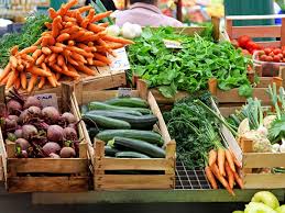 Fresh carrots, beets, cucumbers, leafy greens, herbs, and other locally grown produce displayed in wooden crates at a farmers market.
