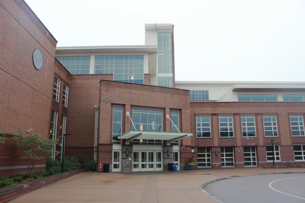 Exterior of Wellesley High School featuring a modern red-brick façade, large windows, and the main entrance beneath a covered canopy.