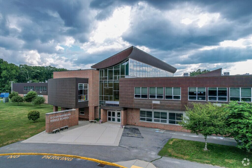 Exterior of Dover-Sherborn Middle School featuring a modern brick-and-glass entrance, landscaped grounds, and a dramatic cloudy sky.