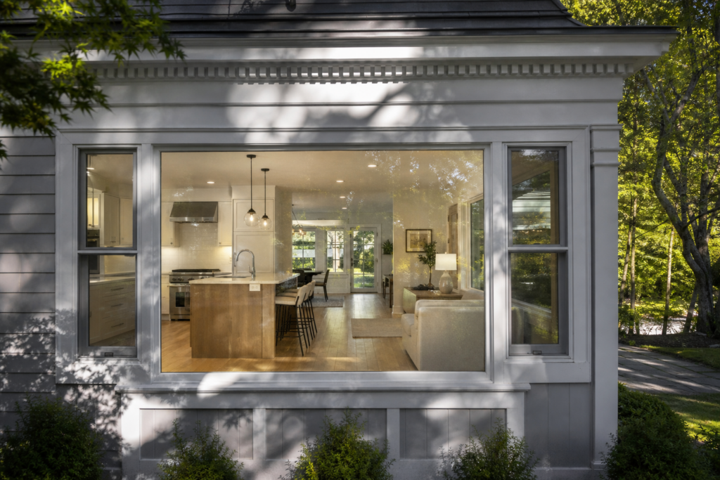 View through a large picture window into an open concept kitchen and living area in Needham, MA